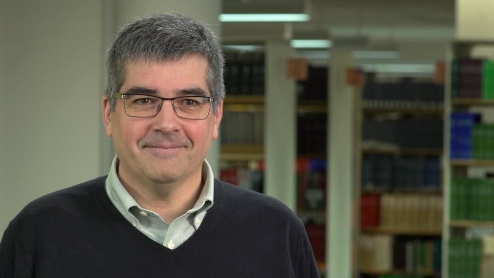 John Cranfield smiles, bookshelves behind him