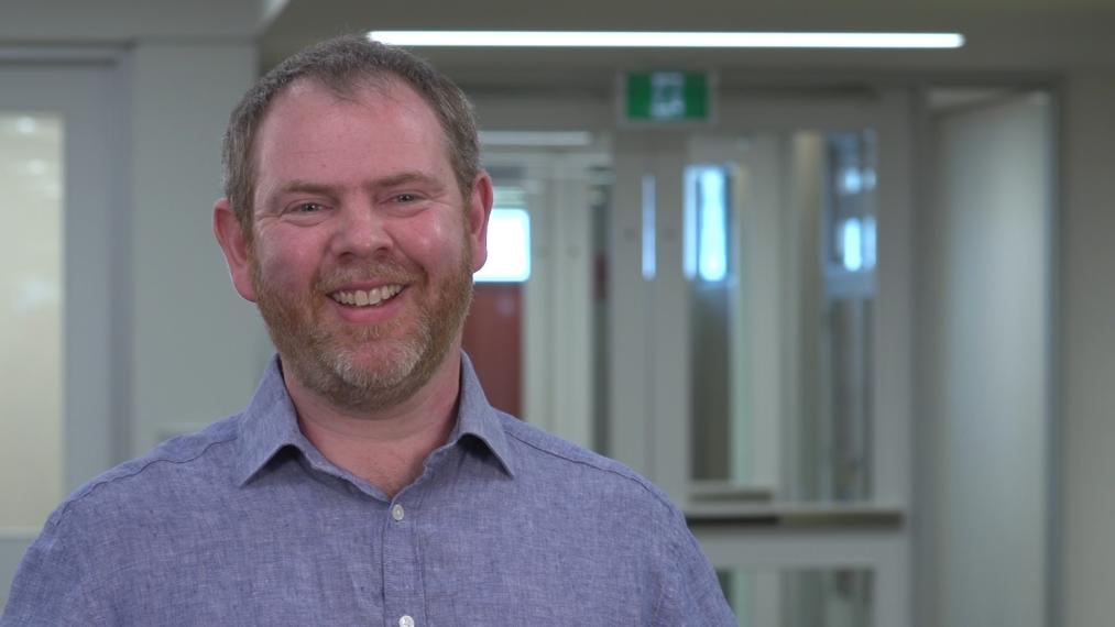 Nigel Raine smiling in front of glass doors