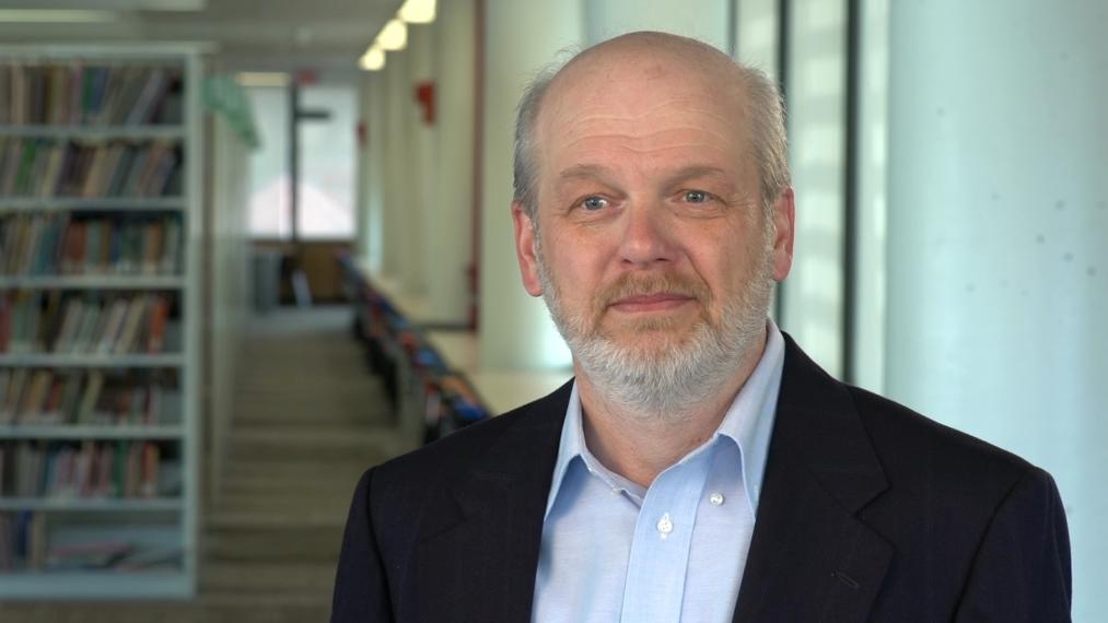 Paul Goodwin stands in front of pillar and bookshelf