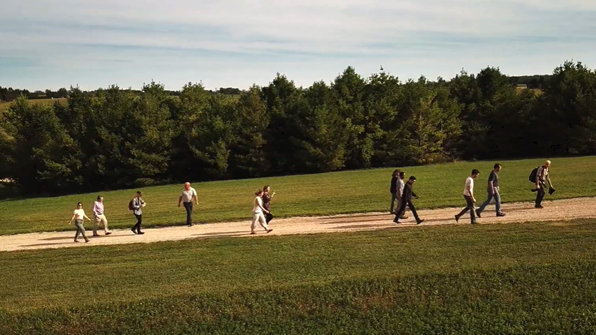 Group of people walking through a path in a green field