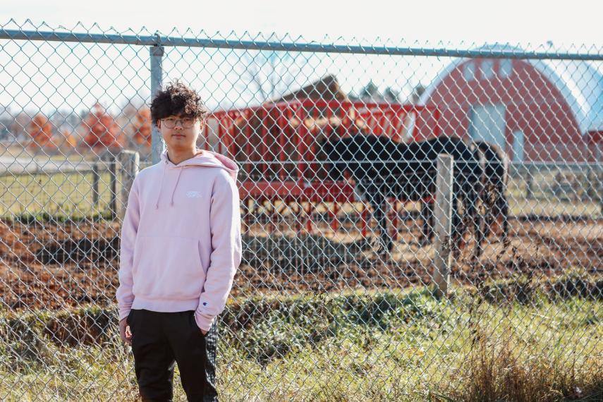 Oswin Lam posed for the camera in front of a fence with horses in the background