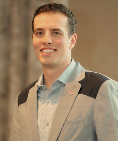 Aaron Lorenz wearing a suit jacket smiling to the camera inside