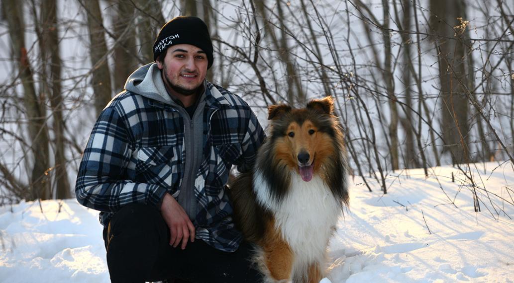 Cameron kneels with his dog Murphy in a snowy woods.