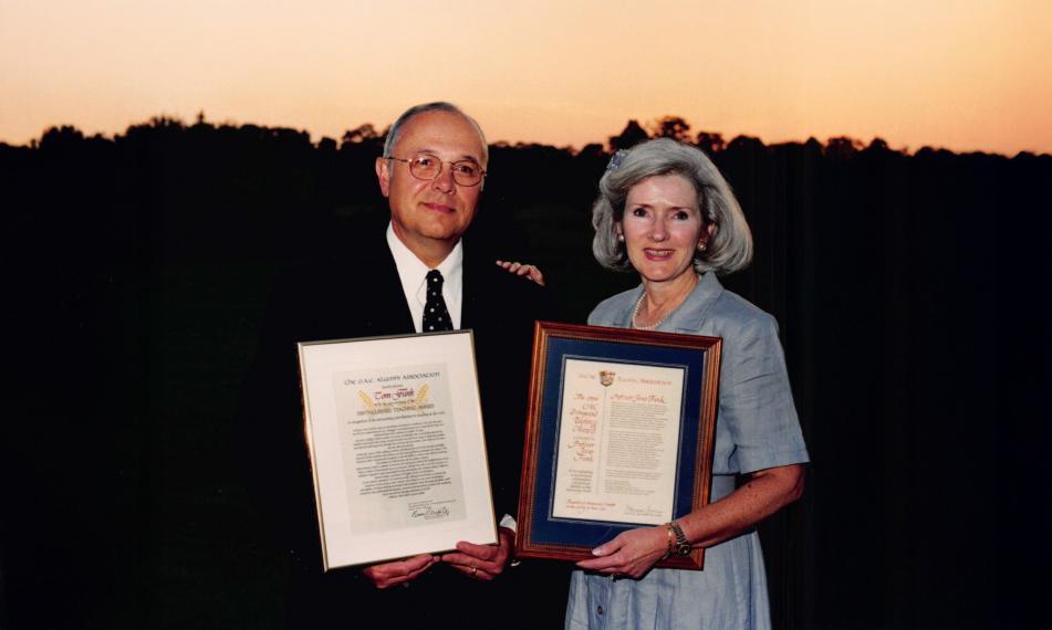 Jane and Tom Funk stand behind a sunset smiling while holding up their Distinguished Teaching Awards (from the OAC)).