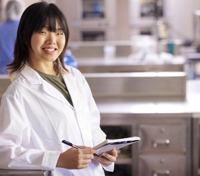 A woman in a white lab coat holding a notebook in a lab.