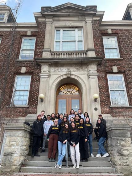 A large group of students stands in front of a beautiful brick building.