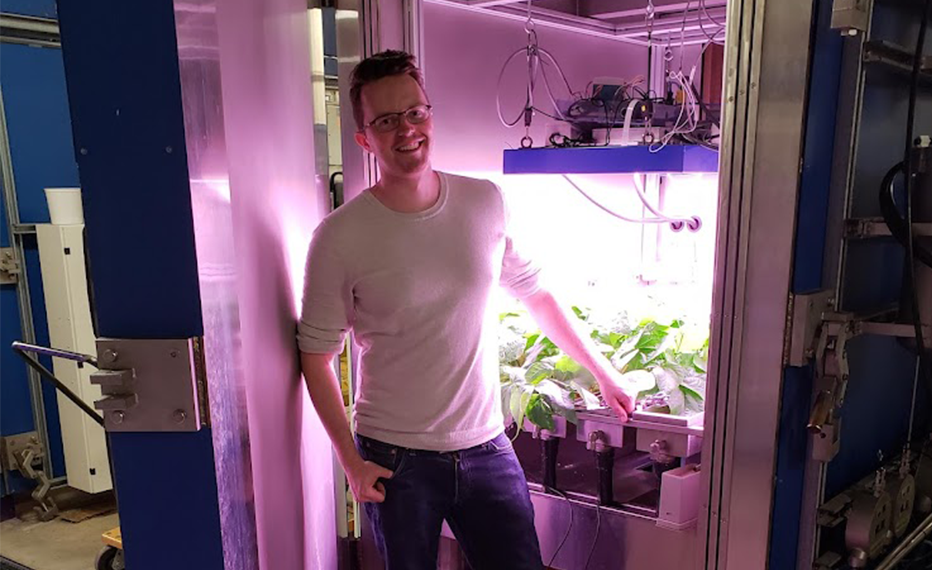 Head shot of Jared Stoochnoff standing in front of a plant growth analysis chamber.