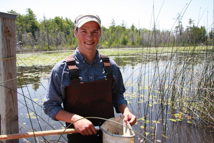 Josh wearing waders and a hat standing in a pond with a net in his hands