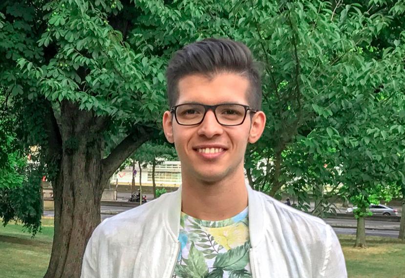 Mehrdad smiles, standing infront of a tree