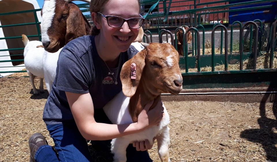 Head shot of Sarah Kay, holding a goat.