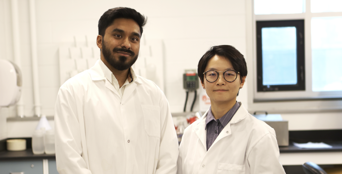Two new faculty members standing in a lab, wearing white lab coats