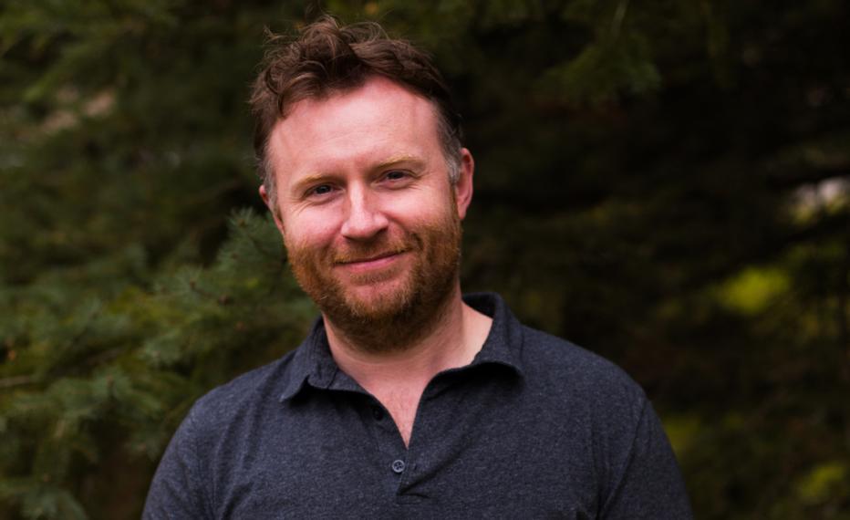 Tom Armitage in dark polo shirt, green trees in background