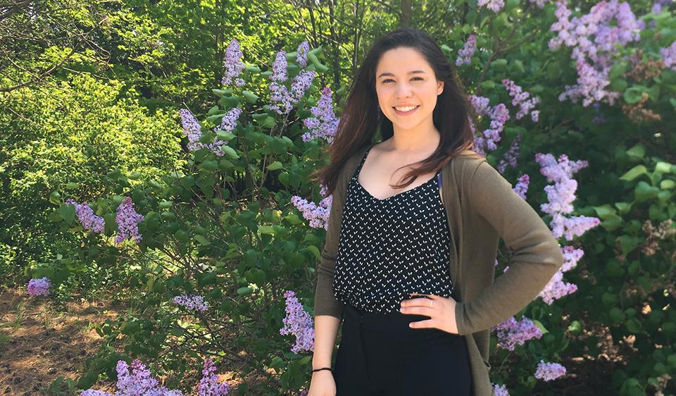 Andrea stands and smiles in front of a flower bush.