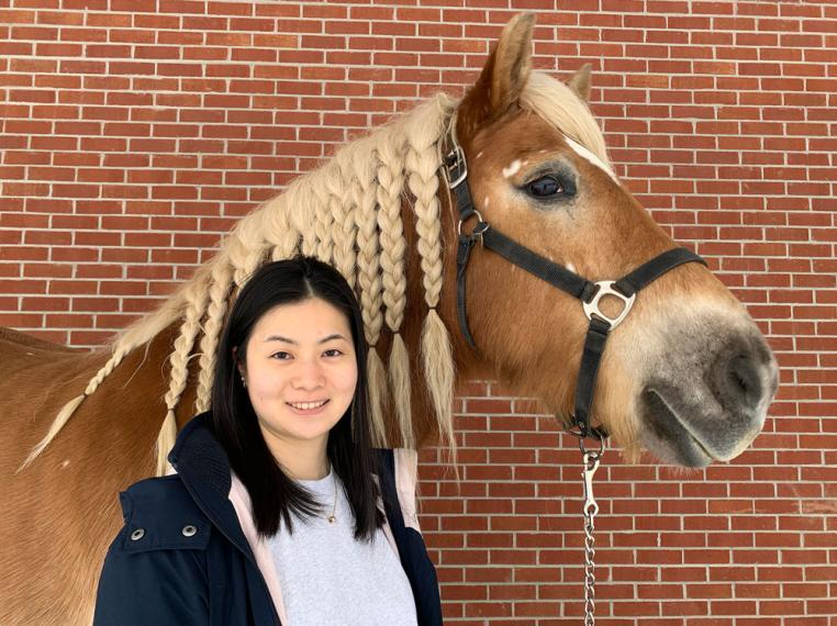 Anna stands with large brown horse whose mane is tied in braids