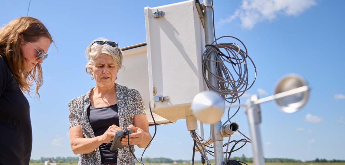 photo of dr. claudia wagner riddle outside in a field inspecting lab equipment with a student looking on