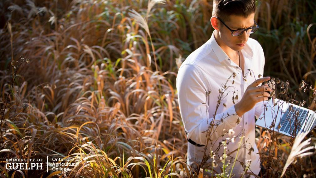 A man stands in a field with an open computer.