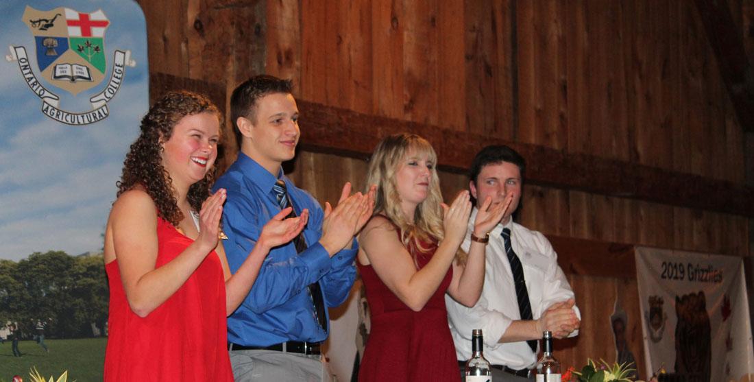 Four students stand up and clap, smiling