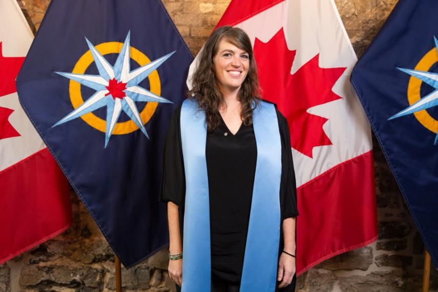 heather schibli standing infront of flags at an award ceremony, wearing a blue sach