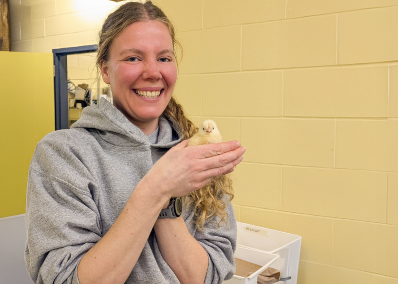 Lea standing in a lab, holding a baby hen