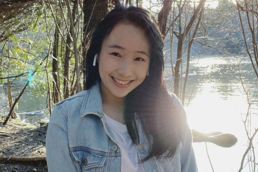 Coey smiles wearing earpods with sun reflecting off a lake behind her