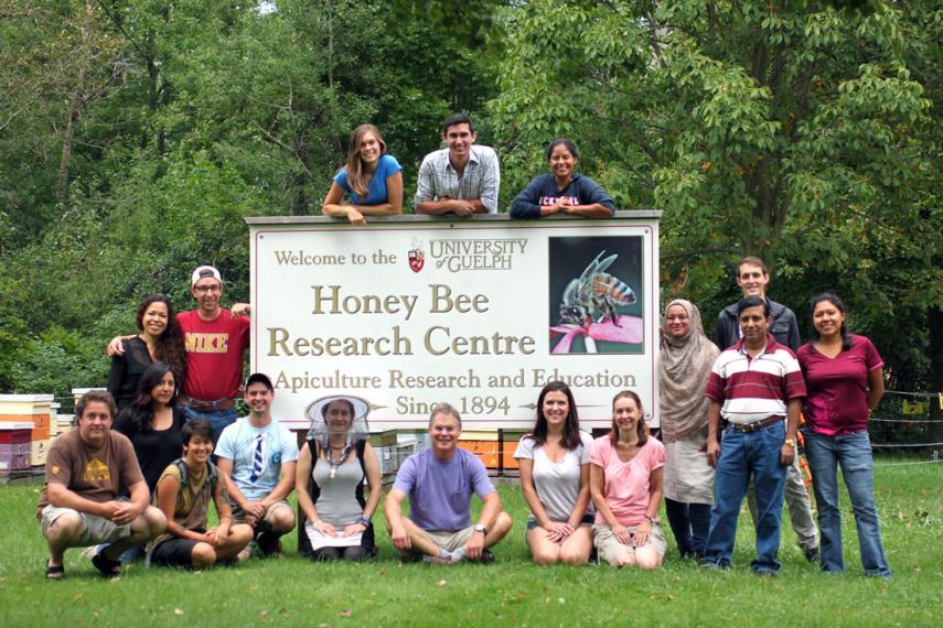 Group of students and faculty stand with large Honey Bee Research Centre sign