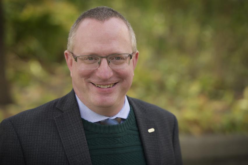 Headshot photo of Prof. Jon Warland with green leaves behind him