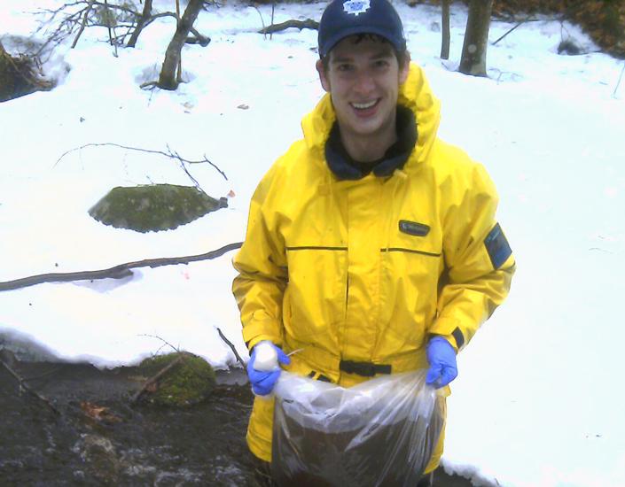 Jordan outside in yellow rain jacket holding bag of sample water, snow on ground
