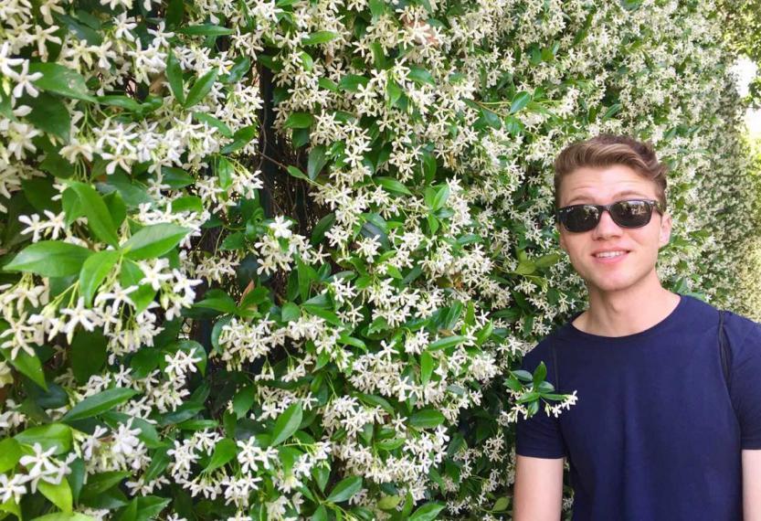 Mark stands infront of a large bush covered in white flowers.