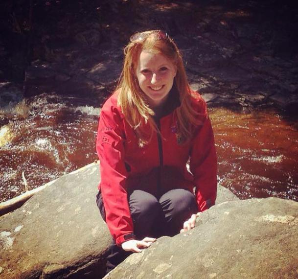 Marnie wearing red jacket and crouching by rocks and a stream of water