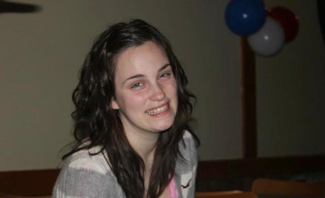Megan wearing grey and white sweater, a couple of balloons hanging behind her
