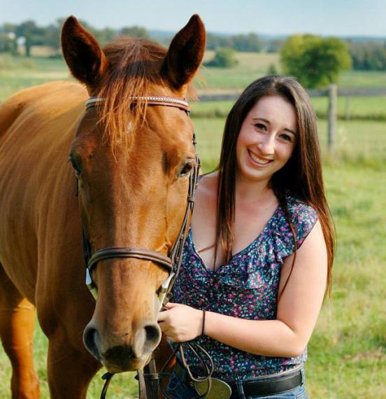 Rachel stands in pasture with large red horse