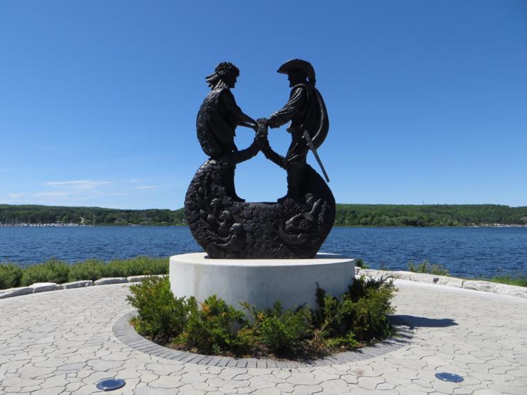Statue of two men shaking hands with blue sky and water in background
