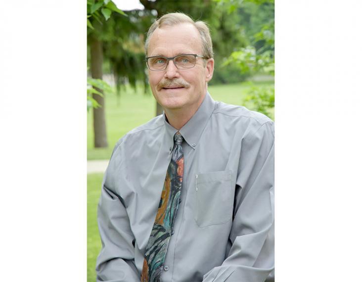 Portrait of Peter Sikkema sitting down and smiling with trees behind him.