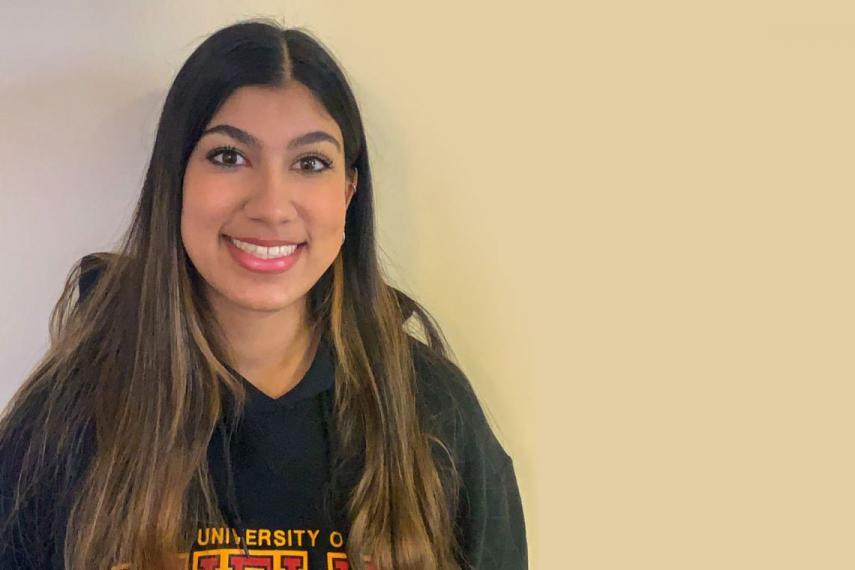 Wafa smiles with U of G hoodie on, yellow wall behind her