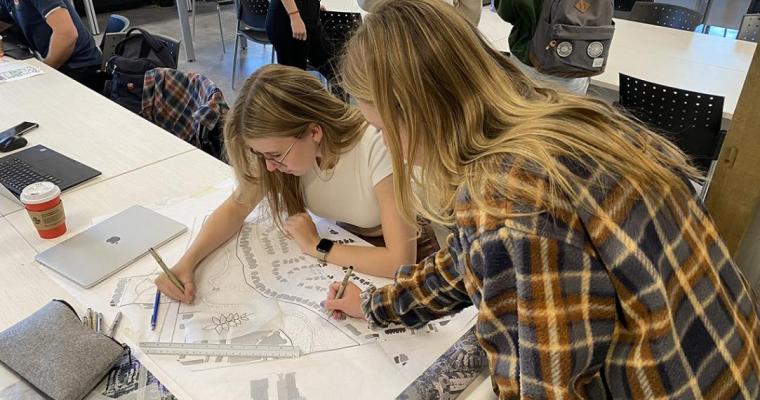 Two female students with long blonde hair working on a landscape architecture project.