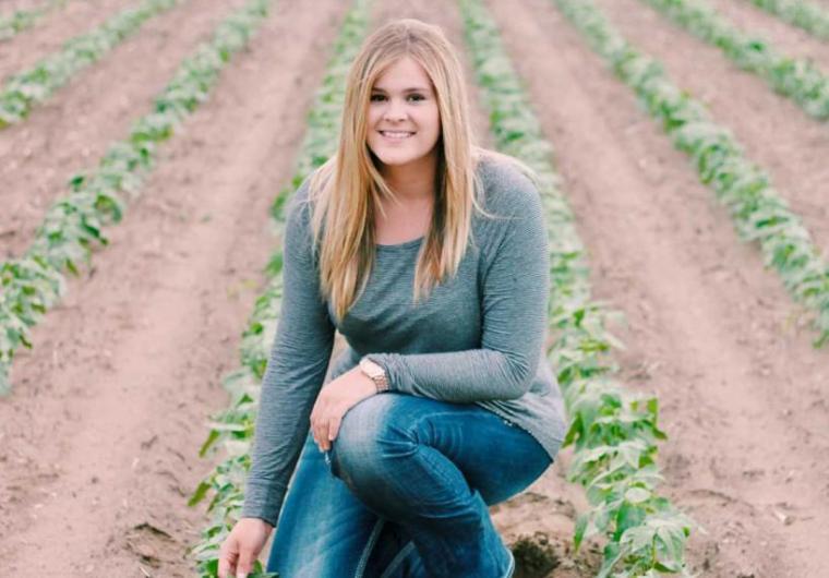 Amy kneels in a farmer's field.