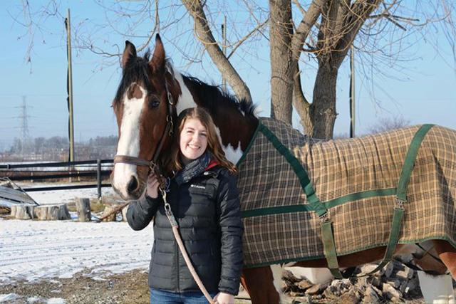 Caleigh outside in winter with horse wearing a blanket. 