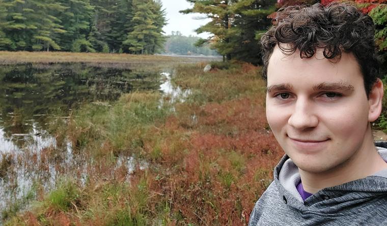 Evan Poncelet, standing beside a body of water, on a camping adventure.