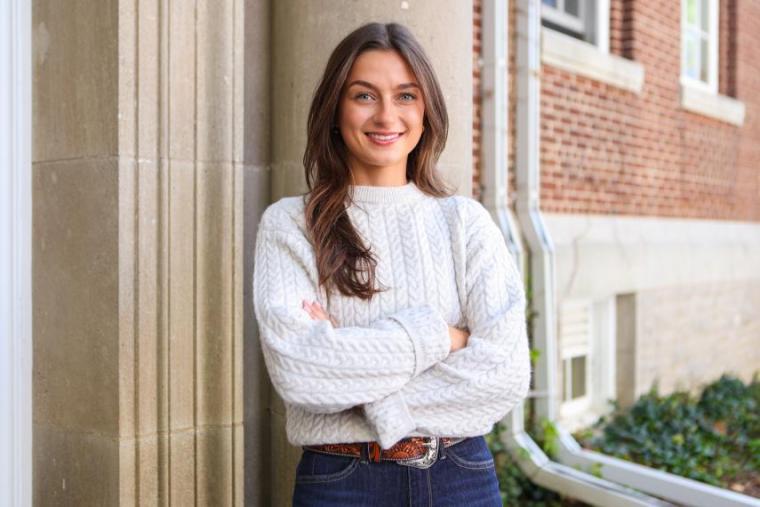a photo of julianna, standing with her arms crossed near a building on campus
