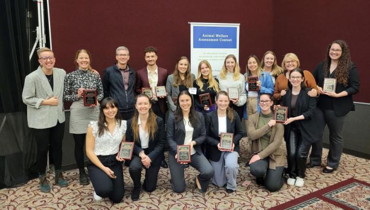 Large group of students stand together smiling holding matching plaques