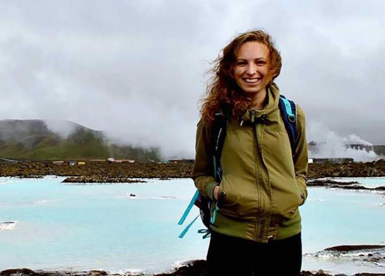 Jamie stands with bright blue lake and mountains behind her. 