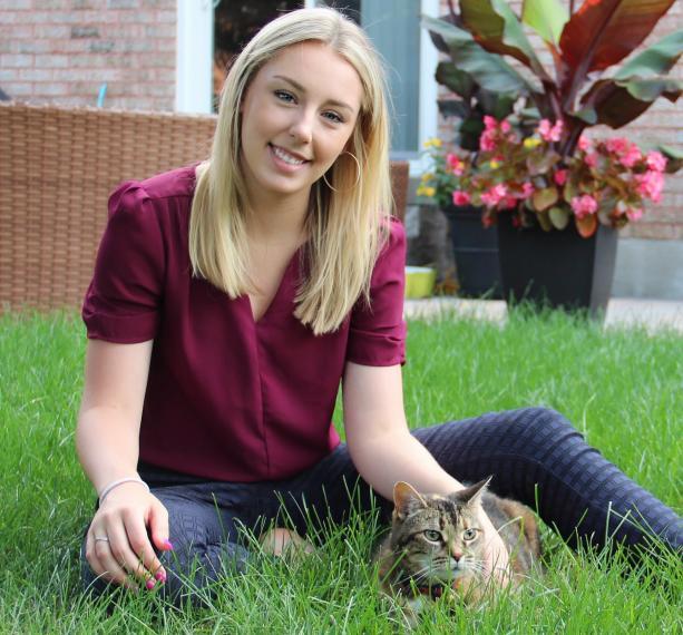 Natalie sits in a yard with a cat.