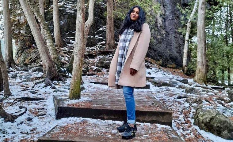 Heat shot of Nidhi standing on stairs surrounded by trees.