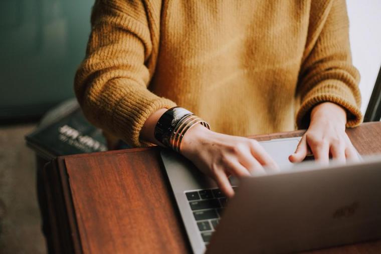 A person in a yellow sweater and gold bracelets typing on a laptop.