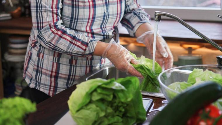 A person washing lettuce in a kitchen sink.