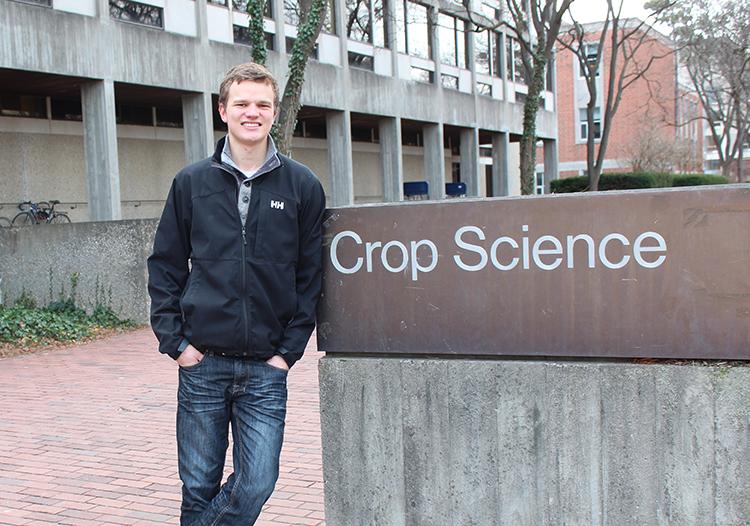 Chris stands outside in jacket beside a sign saying "Crop Science"