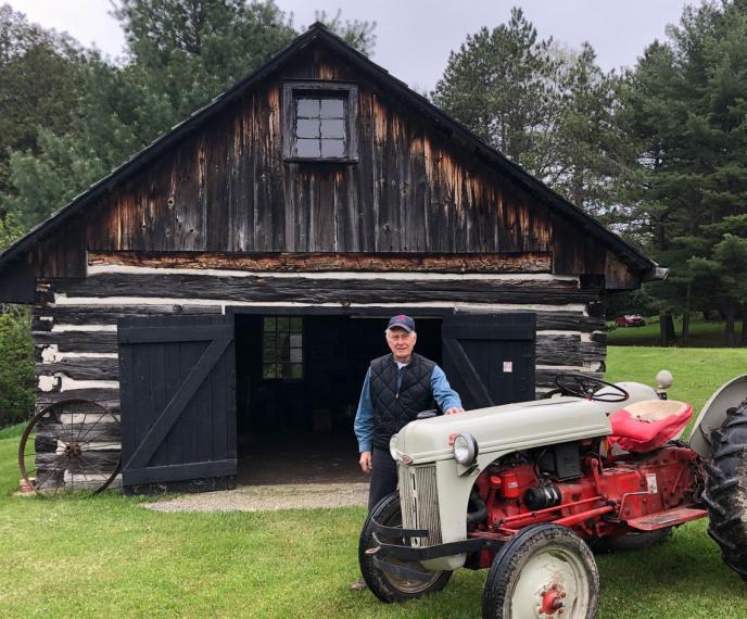 Dave Little standing behnd a red tractor and in front of a log shed