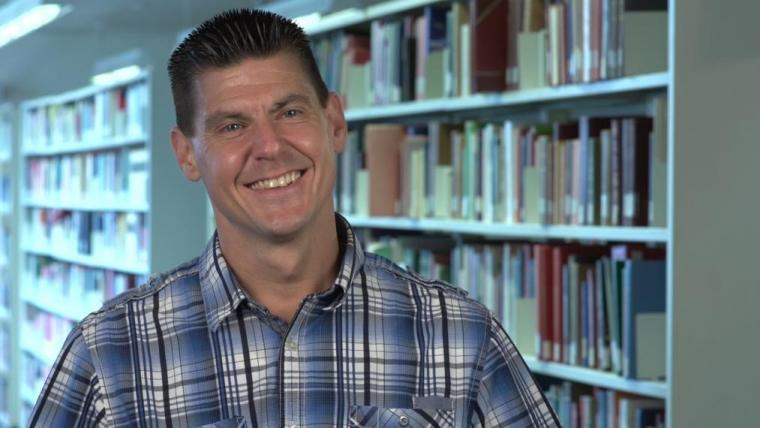 Trevor DeVries smiling and standing in front of a wall of books.