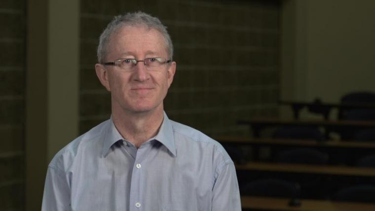 Wayne Caldwell headshot sitting in dark lecture room