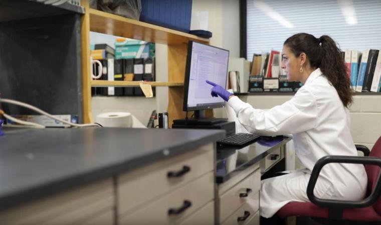 Prof. Angela Canovas sits in lab coat looking at computer screen